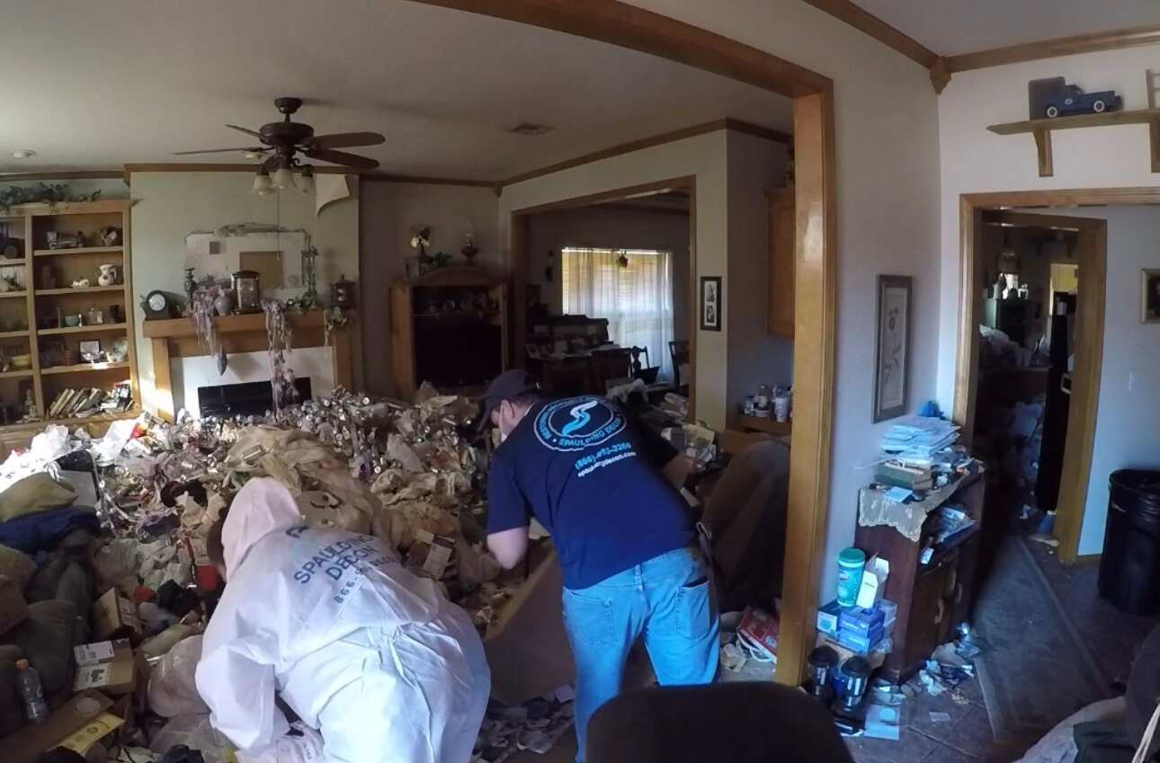 Spaulding Decon team members cleaning a disorganized living room, addressing hoarding and biohazard issues in Oklahoma City