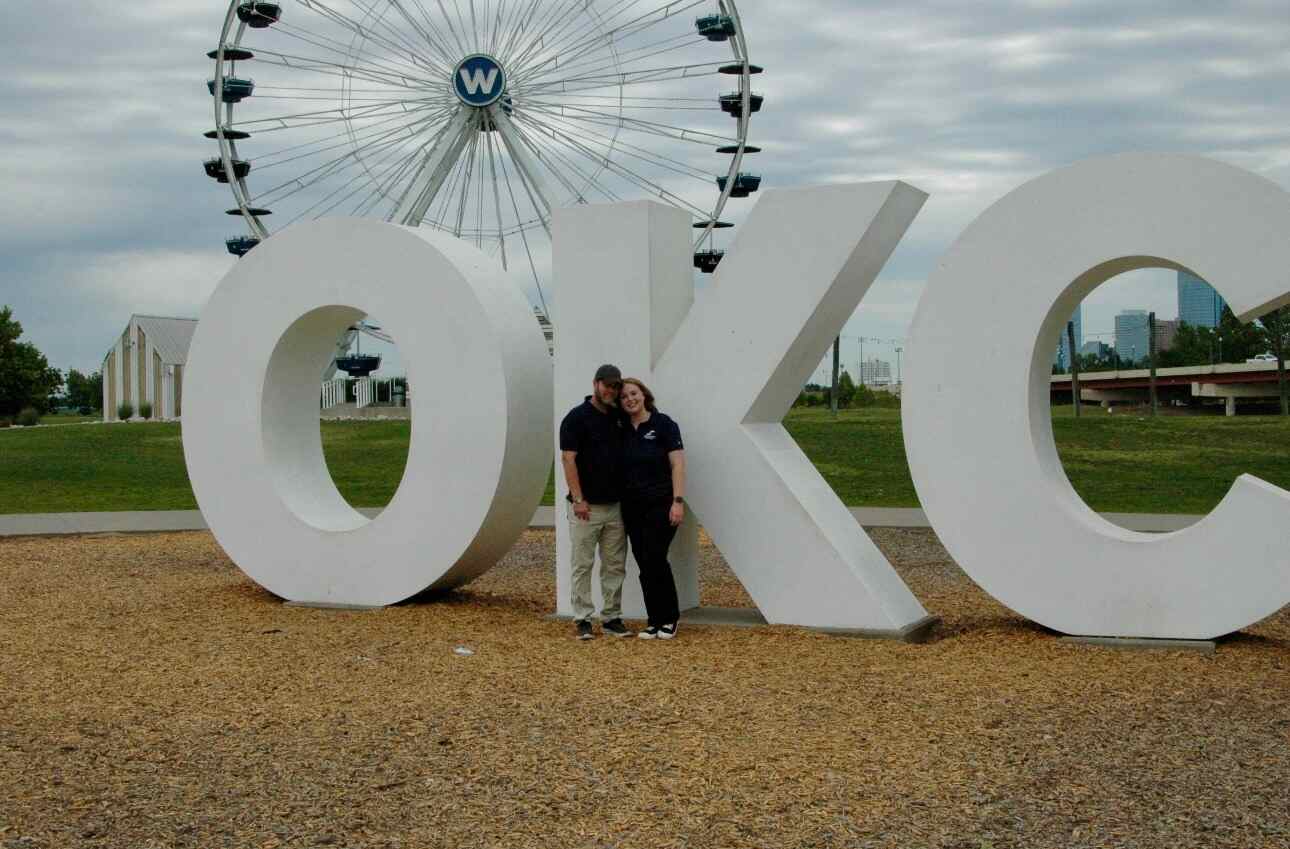 Hannah Oden and Shane Welch, owners of Spaulding Decon Oklahoma City, posing inside the large white OKC sign at the Wheeler Ferris Wheel plaza in OKC's Wheeler District
