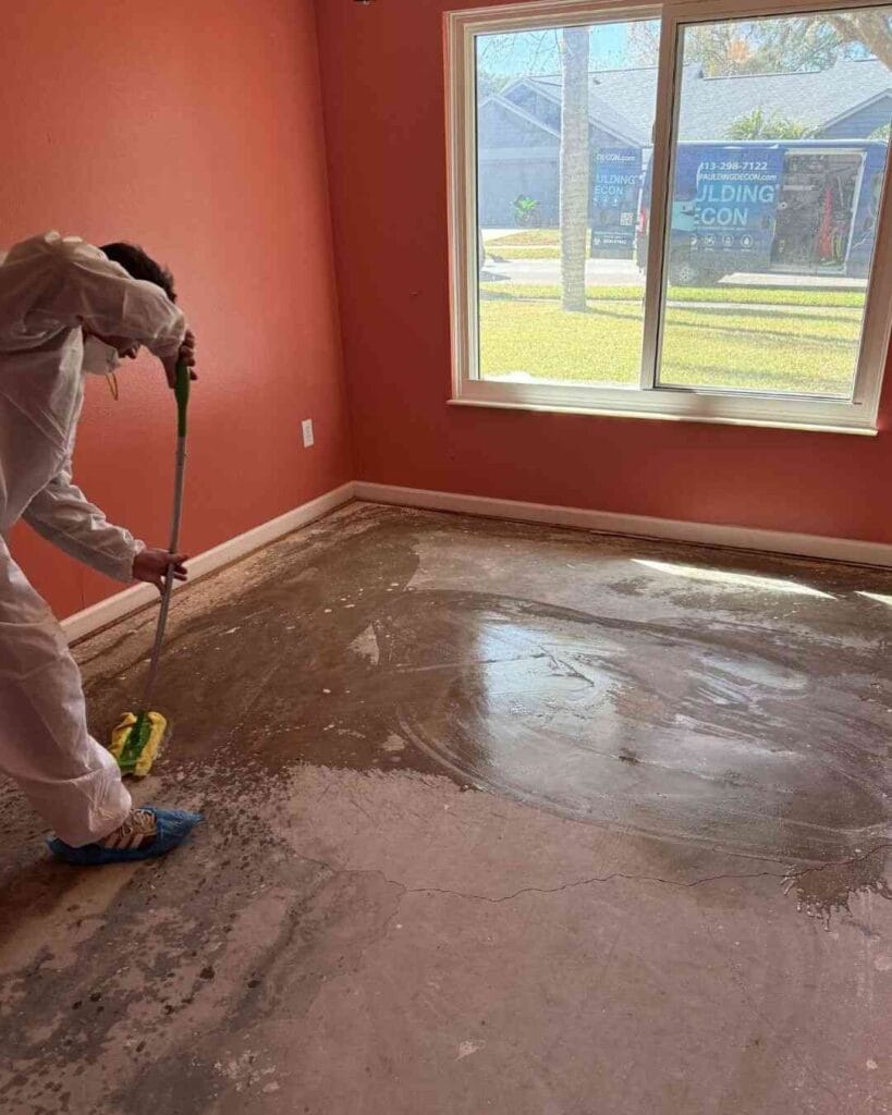 A Spaulding Decon technician in full PPE sanitizes a bare concrete subfloor after contaminated flooring materials were removed