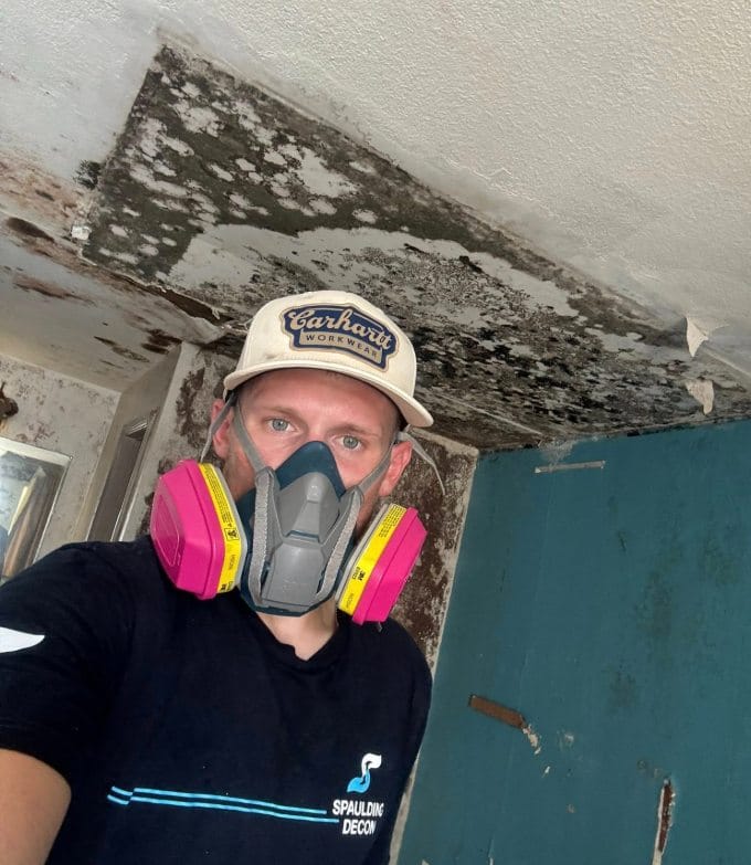Andrew Streacker wearing a protective respirator mask below a ceiling with severe mold damage