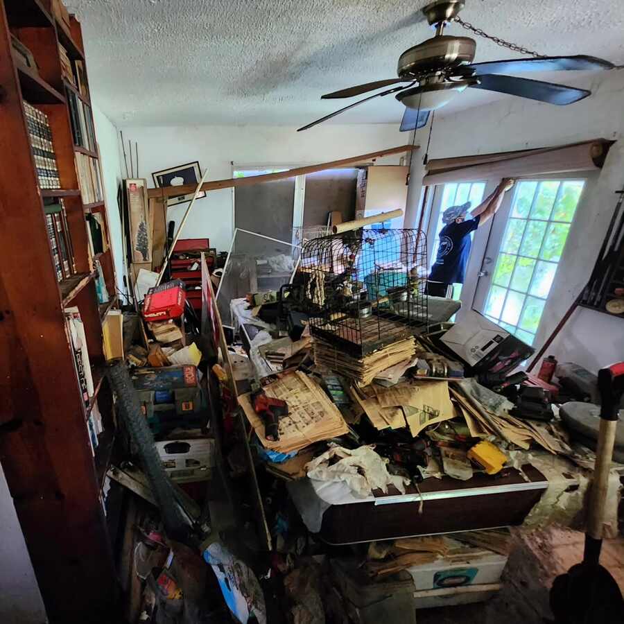 Spaulding Decon Miami technician cleaning a severely cluttered hoarding home filled with stacked newspapers, tools, and personal belongings