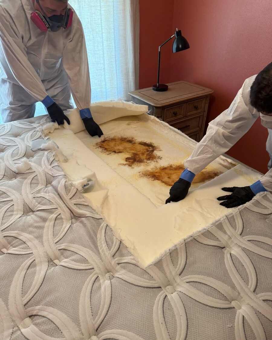 Spaulding Decon Tampa technicians in protective gear removing a biohazard-contaminated mattress during a compassionate cleanup